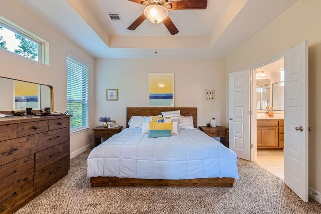 carpeted bedroom featuring ensuite bath, a raised ceiling, and ceiling fan