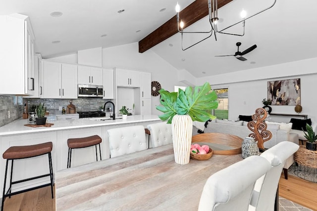 dining area with vaulted ceiling with beams, sink, light wood-type flooring, and ceiling fan with notable chandelier