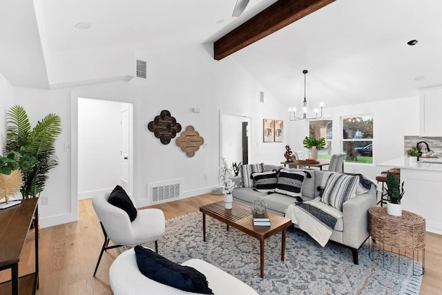 living room with vaulted ceiling with beams, light wood-type flooring, sink, and an inviting chandelier