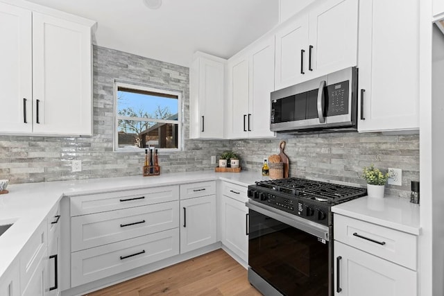 kitchen with white cabinets, decorative backsplash, stainless steel appliances, and light hardwood / wood-style flooring