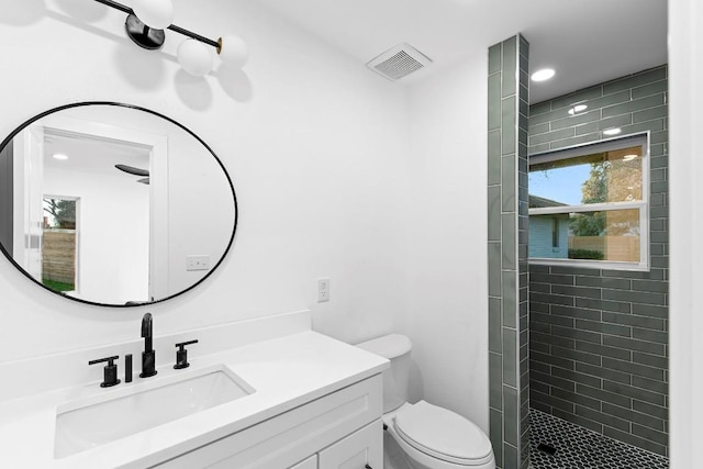 bathroom with tiled shower, vanity, and toilet