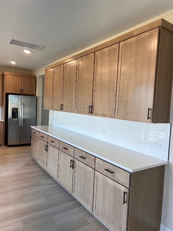 128 Alistair Dr, Georgetown, TX 78633 - kitchen featuring stainless steel fridge with ice dispenser, light wood finished floors, tasteful backsplash, light countertops, and a textured ceiling