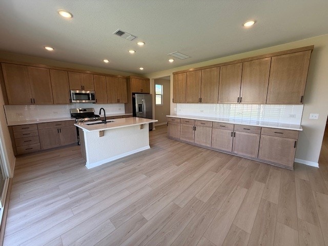 128 Alistair Dr, Georgetown, TX 78633 - kitchen with appliances with stainless steel finishes, light countertops, a center island with sink, backsplash, and light wood-style floors