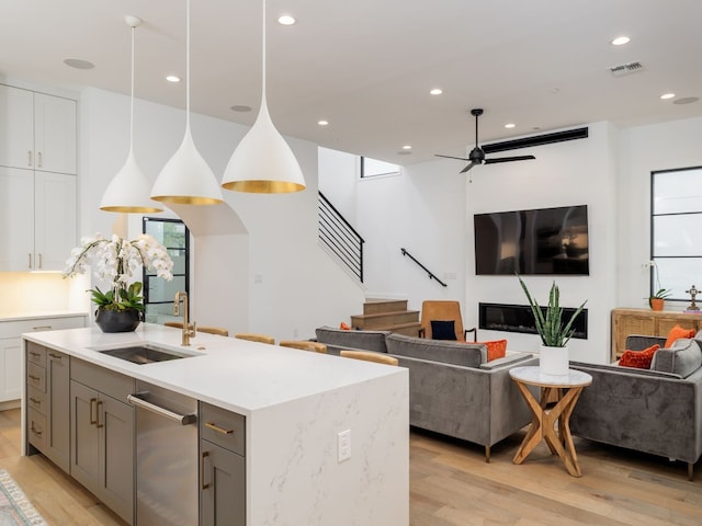 kitchen with white cabinets, sink, hanging light fixtures, light hardwood / wood-style flooring, and ceiling fan