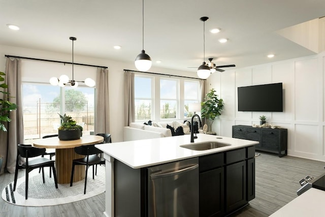 kitchen featuring dishwasher, sink, hanging light fixtures, light wood-type flooring, and an island with sink