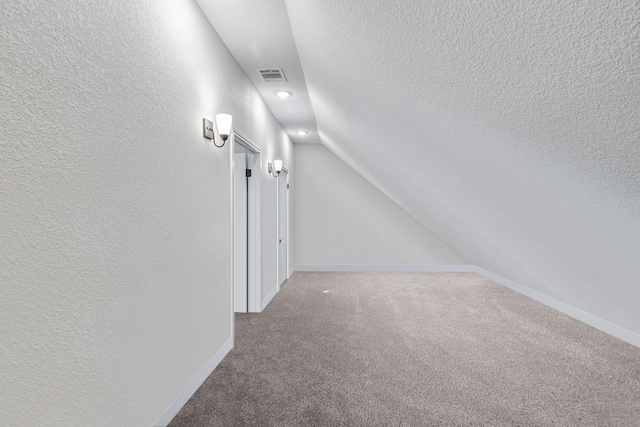 corridor with lofted ceiling, carpet, and a textured ceiling