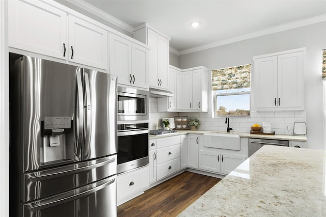 kitchen with appliances with stainless steel finishes, crown molding, white cabinetry, and light stone countertops