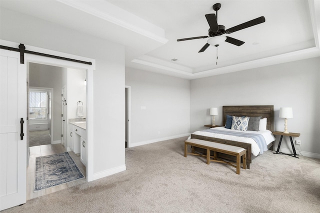 carpeted bedroom with ceiling fan, a tray ceiling, ensuite bath, and a barn door