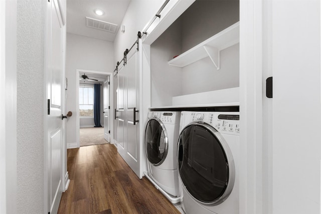 clothes washing area with ceiling fan, washer and clothes dryer, dark hardwood / wood-style floors, and a barn door