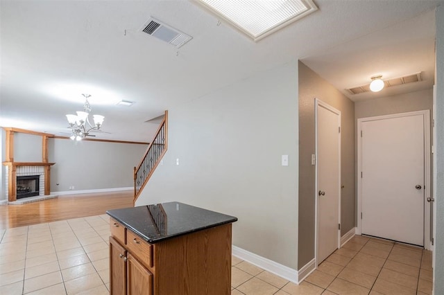 kitchen featuring a notable chandelier, dark stone countertops, pendant lighting, a fireplace, and light tile patterned flooring