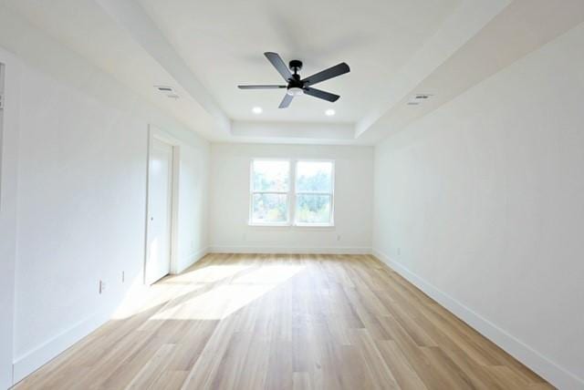 unfurnished room featuring ceiling fan, a tray ceiling, and light hardwood / wood-style flooring