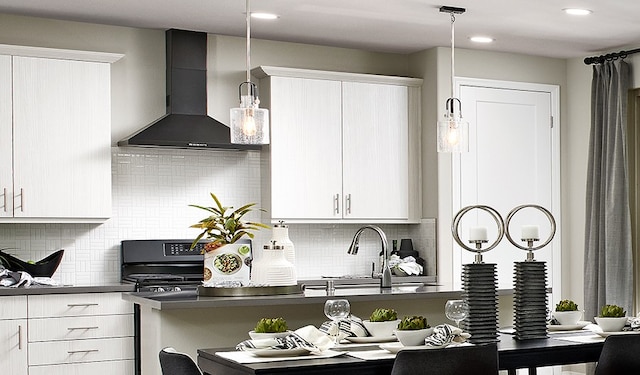 kitchen with white cabinetry, hanging light fixtures, wall chimney range hood, and range