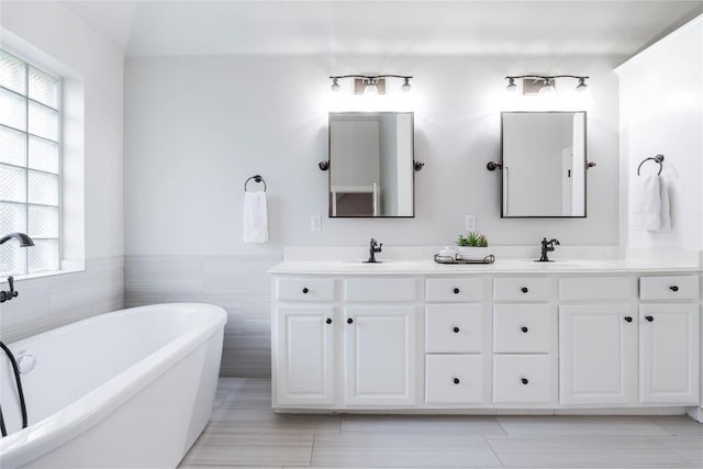 504 River Down Rd, Georgetown, TX 78628 - bathroom with plenty of natural light, a freestanding bath, double vanity, tile walls, and wainscoting