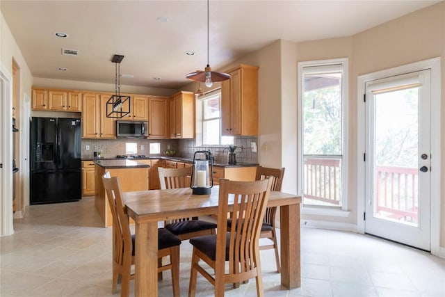 kitchen with decorative backsplash, black fridge, hanging light fixtures, and a wealth of natural light