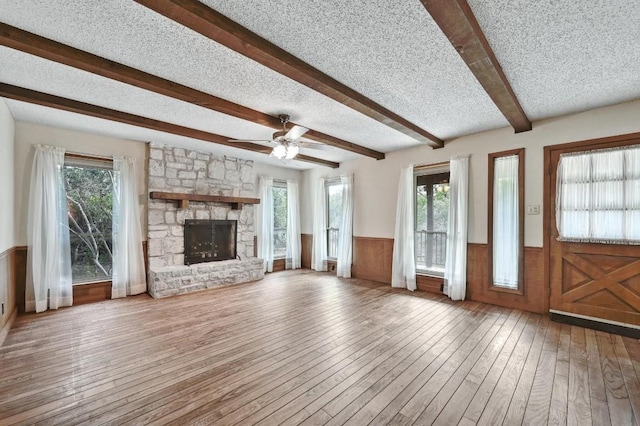 13000 Grubstake Gulch St, Bee Cave, TX 78738 - unfurnished living room featuring wainscoting, wood-type flooring, beamed ceiling, ceiling fan, and a stone fireplace