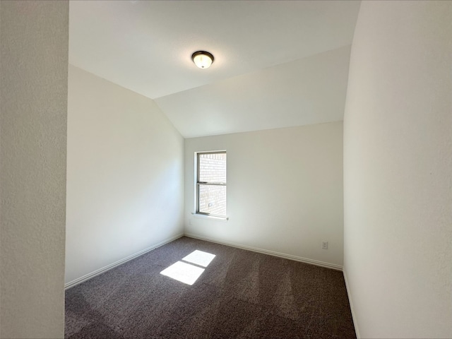 empty room featuring lofted ceiling, dark carpet, and baseboards