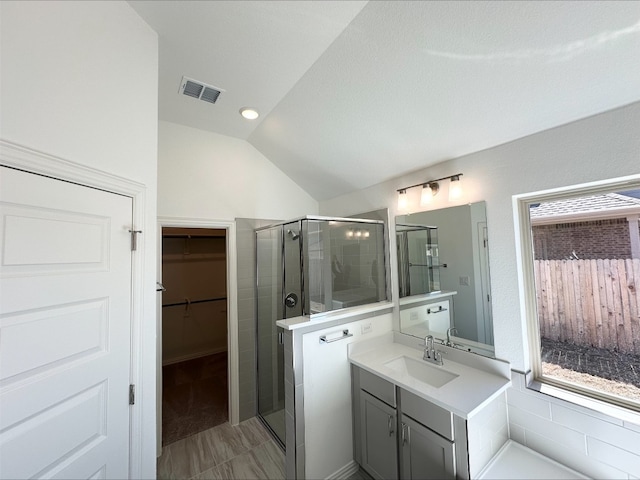 bathroom featuring a walk in closet, visible vents, a stall shower, vaulted ceiling, and vanity