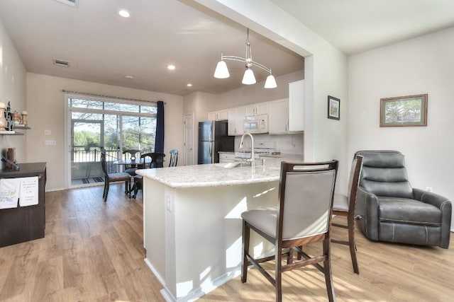 kitchen with white appliances, a kitchen breakfast bar, white cabinetry, pendant lighting, and a sink