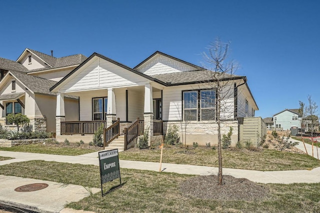 144 Adelton Blvd, Bastrop, TX 78602 - view of front facade with stone siding, a porch, roof with shingles, and a front lawn