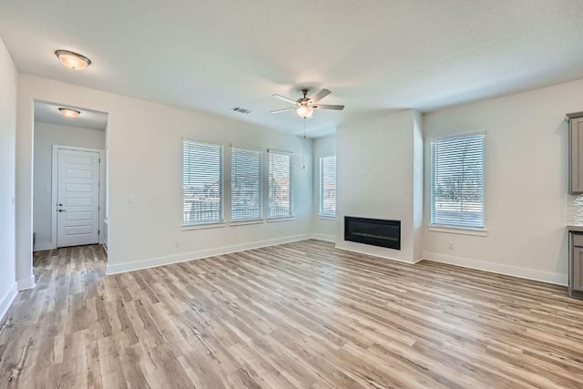 unfurnished living room featuring a wealth of natural light, visible vents, light wood-style flooring, and a ceiling fan
