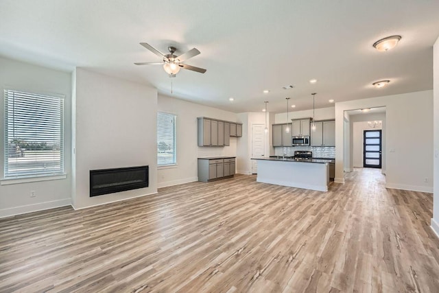 unfurnished living room with baseboards, light wood-style floors, a fireplace, and ceiling fan