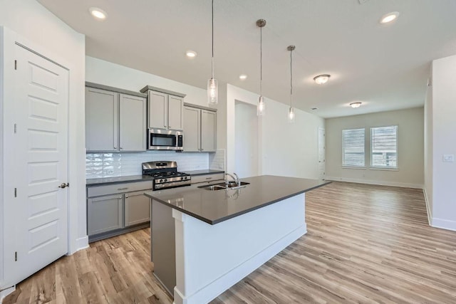kitchen with a sink, light wood finished floors, appliances with stainless steel finishes, gray cabinetry, and decorative backsplash