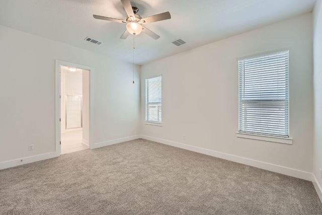 carpeted spare room featuring baseboards, ceiling fan, and visible vents
