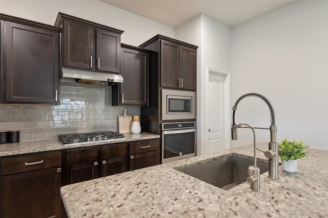 kitchen with light stone countertops, appliances with stainless steel finishes, dark brown cabinets, and sink