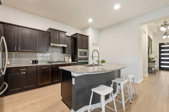 kitchen featuring appliances with stainless steel finishes, tasteful backsplash, sink, light hardwood / wood-style flooring, and an island with sink