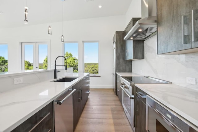 kitchen featuring sink, wall chimney exhaust hood, light hardwood / wood-style floors, pendant lighting, and appliances with stainless steel finishes