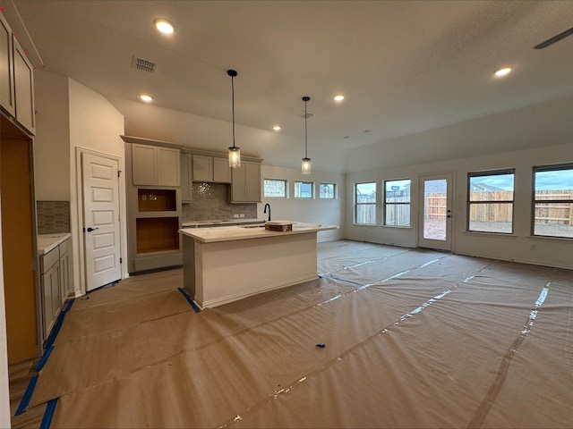 kitchen with decorative backsplash, hanging light fixtures, a kitchen island with sink, and sink