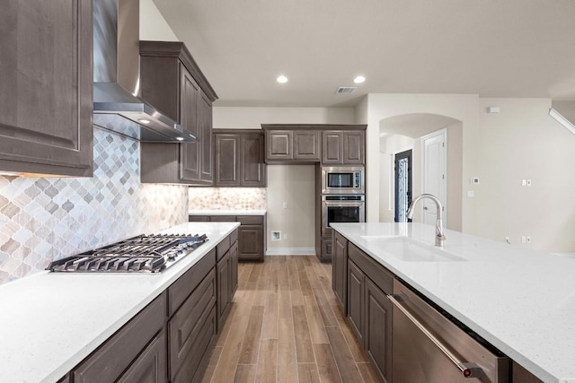 kitchen featuring light stone countertops, light wood-type flooring, stainless steel appliances, sink, and wall chimney range hood