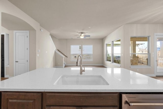 kitchen with light stone counters, stainless steel dishwasher, a kitchen island with sink, and sink