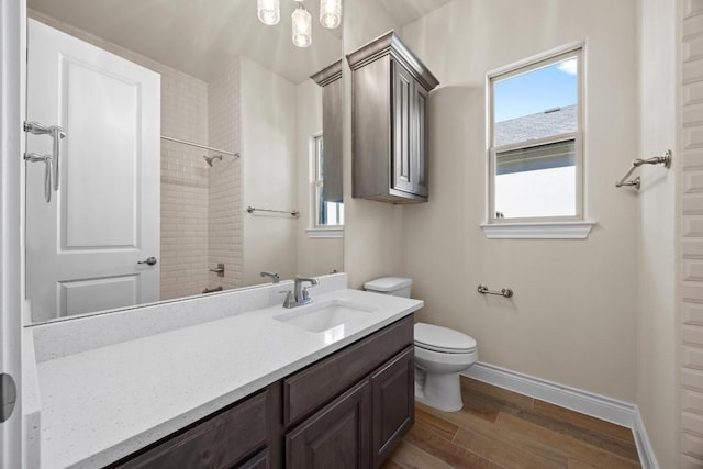 bathroom with hardwood / wood-style flooring, vanity, tiled shower, and toilet