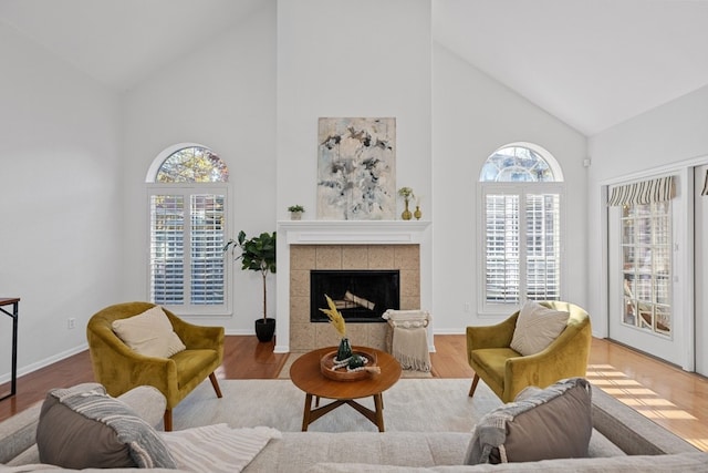 living area with high vaulted ceiling, baseboards, a tiled fireplace, and wood finished floors