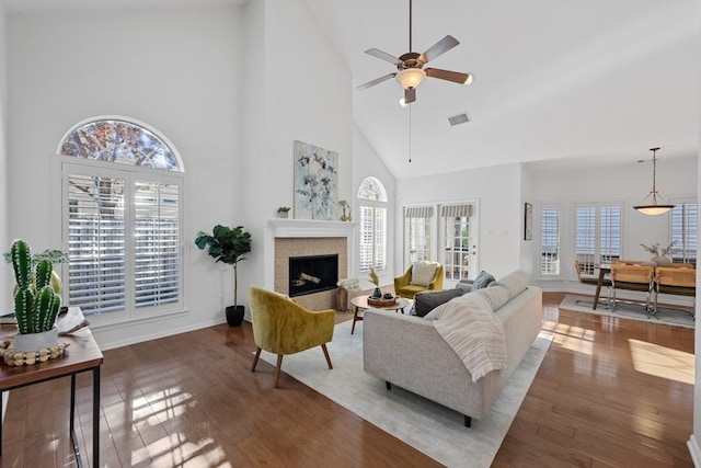 living room with ceiling fan, a tiled fireplace, visible vents, and hardwood / wood-style floors