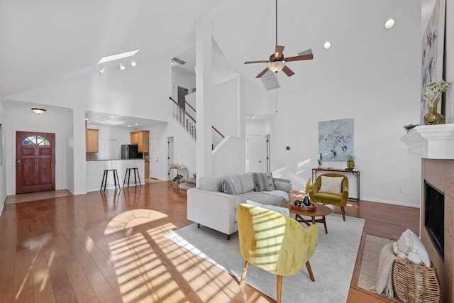 living room featuring high vaulted ceiling, a fireplace, a skylight, stairs, and light wood-type flooring