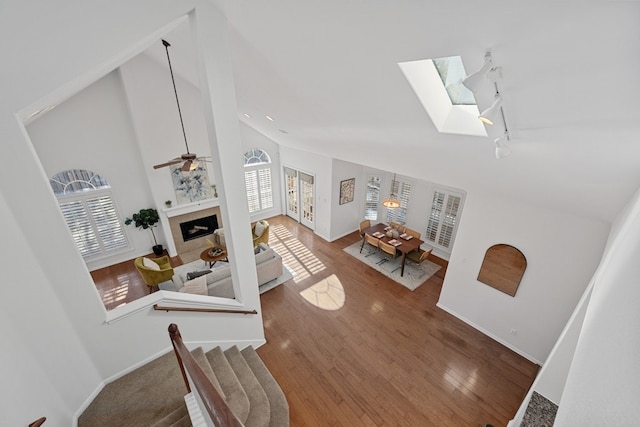 living area with high vaulted ceiling, a tile fireplace, hardwood / wood-style flooring, a skylight, and baseboards