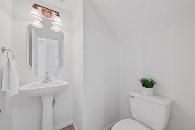 half bathroom with lofted ceiling, baseboards, and toilet