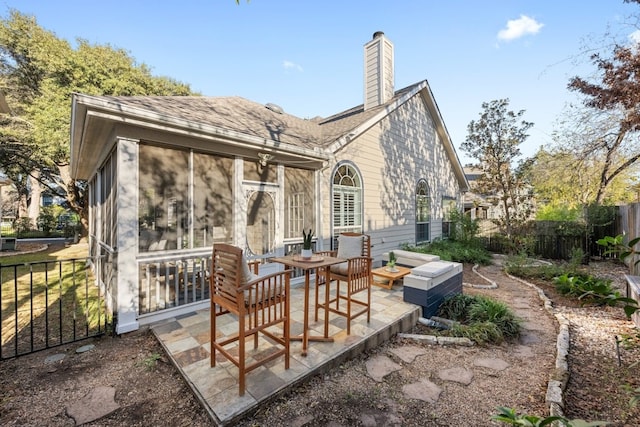 back of house featuring roof with shingles, a patio, a chimney, a sunroom, and fence