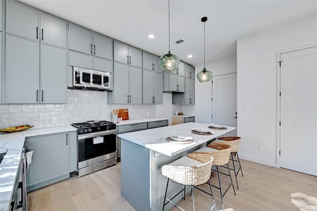 kitchen with appliances with stainless steel finishes, a kitchen breakfast bar, tasteful backsplash, decorative light fixtures, and a center island