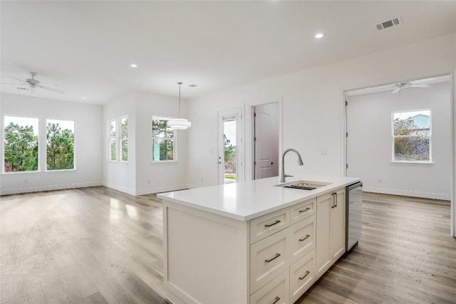 kitchen featuring dishwasher, a kitchen island with sink, hanging light fixtures, sink, and light hardwood / wood-style flooring