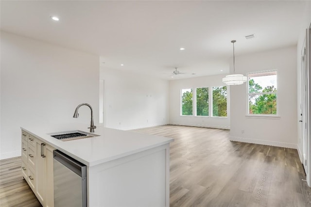 kitchen with a kitchen island with sink, hanging light fixtures, sink, light hardwood / wood-style floors, and white cabinetry