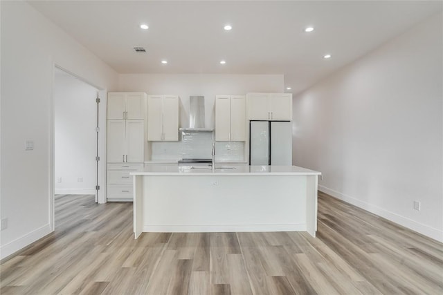 kitchen with a center island with sink, wall chimney exhaust hood, white fridge, and white cabinets