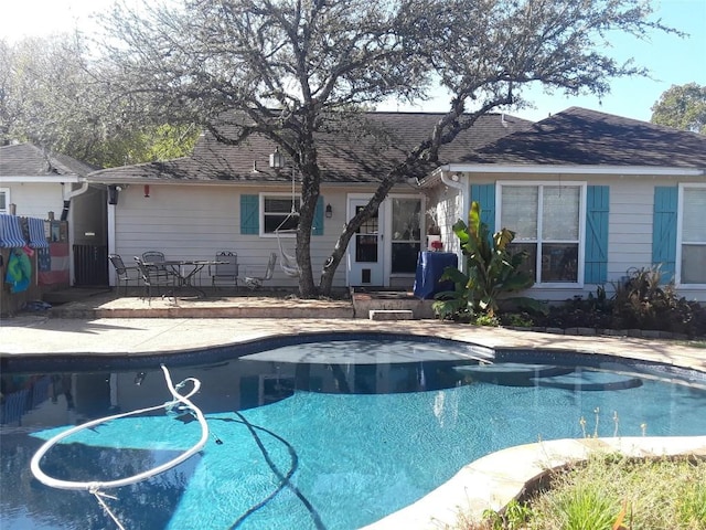 back of house featuring a patio, an outdoor pool, and roof with shingles
