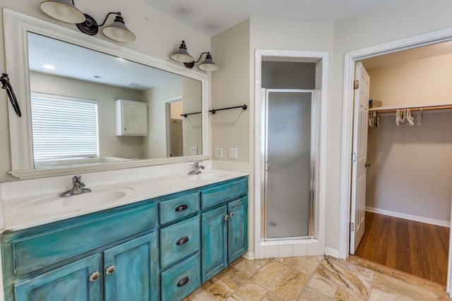 bathroom featuring a sink, a walk in closet, a shower stall, and double vanity