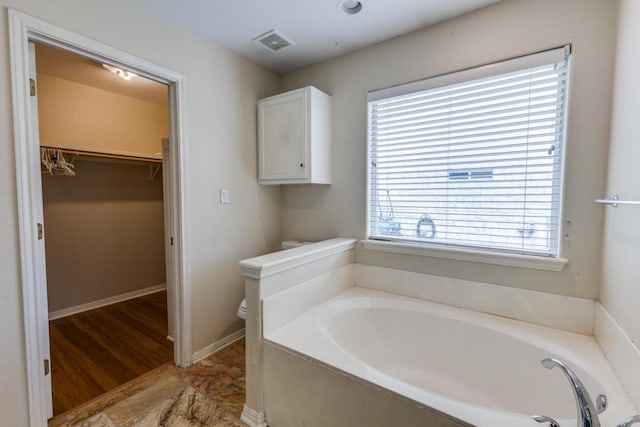 bathroom with a spacious closet, a garden tub, toilet, and visible vents