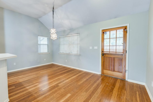 unfurnished dining area with baseboards, an inviting chandelier, wood finished floors, and vaulted ceiling