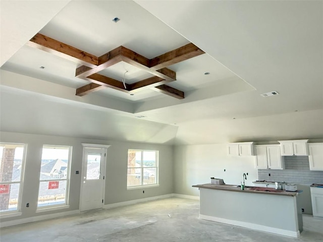 kitchen with sink, tasteful backsplash, beamed ceiling, a kitchen island with sink, and white cabinets