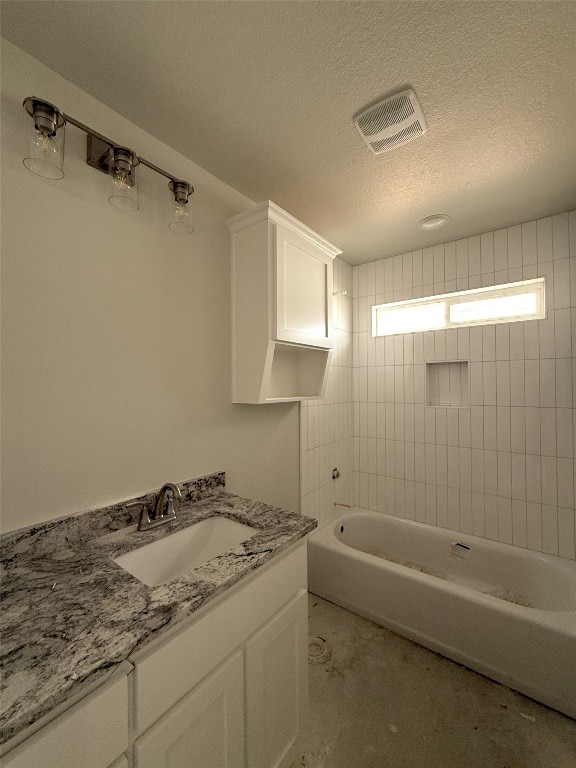 bathroom with tiled shower / bath combo, vanity, and a textured ceiling